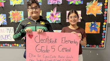 Two elementary students stand holding a poster about the Cereal Drive