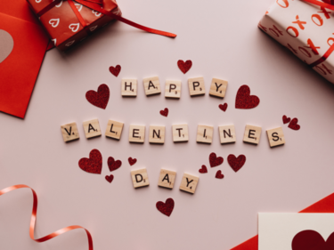 Happy Valentines Day written with scrabble letters with valentines decor around it on a table