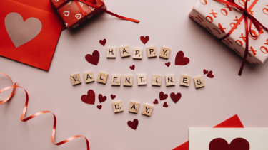 Happy Valentines Day written with scrabble letters with valentines decor around it on a table