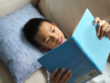 Child reading a blue book on a beige couch 
