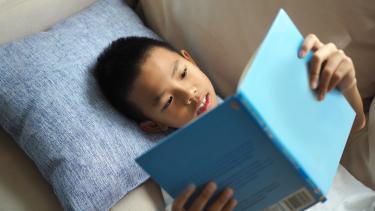 Child reading a blue book on a beige couch 