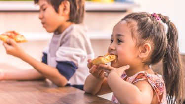 Kids eating pizza a boy and girl sitting on a wooden table next to each other eating pizza