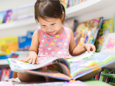 Small girl reading a book cross legged on the floor of a library