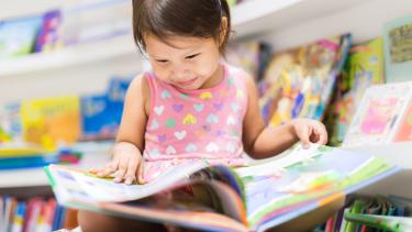 Small girl reading a book cross legged on the floor of a library