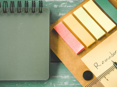 Reminder on sticky note pad sitting on a green table with a green notebook beside it