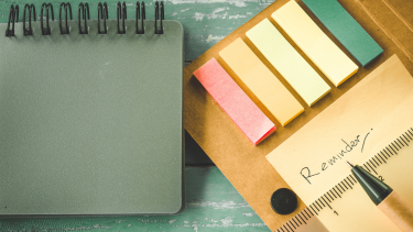 Reminder Reminder on sticky note pad sitting on a green table with a green notebook beside it