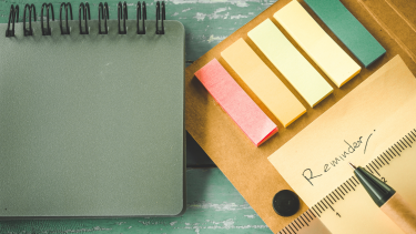 Reminder on sticky note pad sitting on a green table with a green notebook beside it