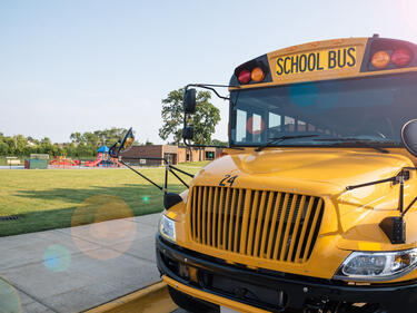 School Bus parked by sidewalk in front of a green field and school