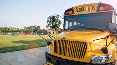School Bus parked by sidewalk in front of a green field and school