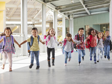 Young students holding hands running down a hallway