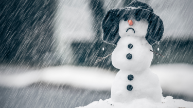 A snowman with a black bucket hat with sleet coming down around it  it