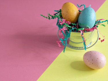 Easter image showing coloured eggs in a chrome basket on a yellow/pink table