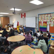 Classroom filled with students and family members sitting at tables